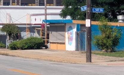 On St. Clair Avenue near East 147th Street, a person in orange bikes down the street and a car drives westbound.