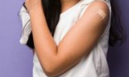 photo of a girl in a white t-shirt showing off her arm with a Band-Aid on it where she recently got a vaccine.