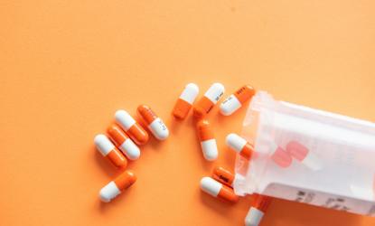 orange and white pill capsules spilling out of a pill bottle onto an orange surface