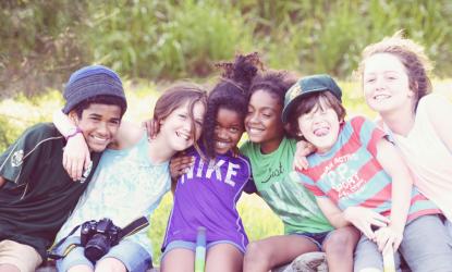 group of six kids sitting outside with their arms around each other.