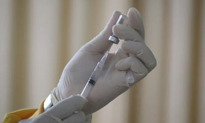 hands in surgical gloves holding a vial and a needle.