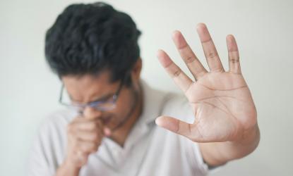 A man sneezing with his other hand out indicating, "stop."