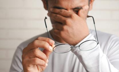 man in a white long sleeve shirt holding his glasses and rubbing his eyes.