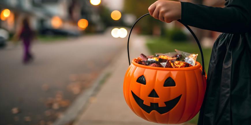 Trick or treater holding a jack-o-lantern filled with candy