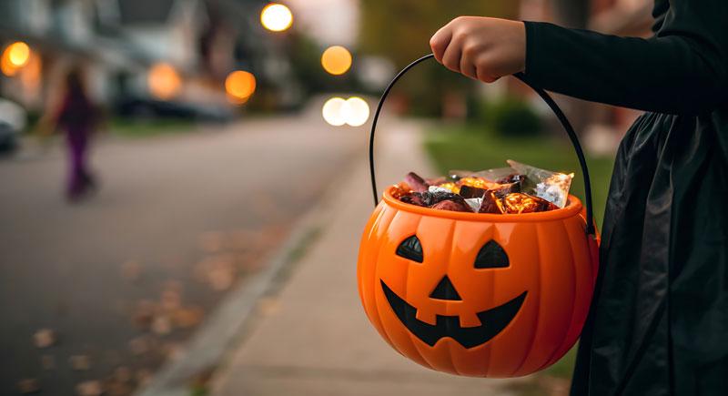 Trick or treater holding a jack-o-lantern filled with candy