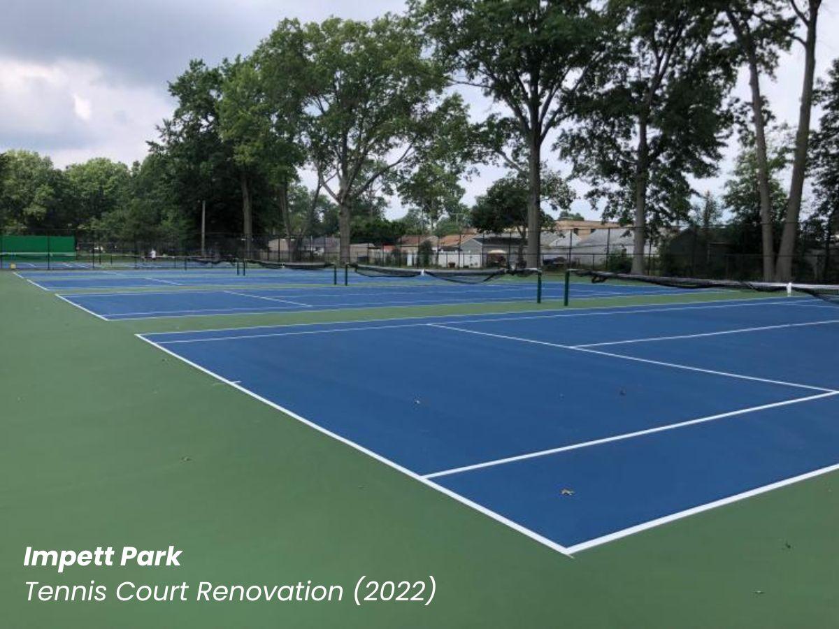 Impett Park tennis court renovation showing a blue and green court with trees in the background.