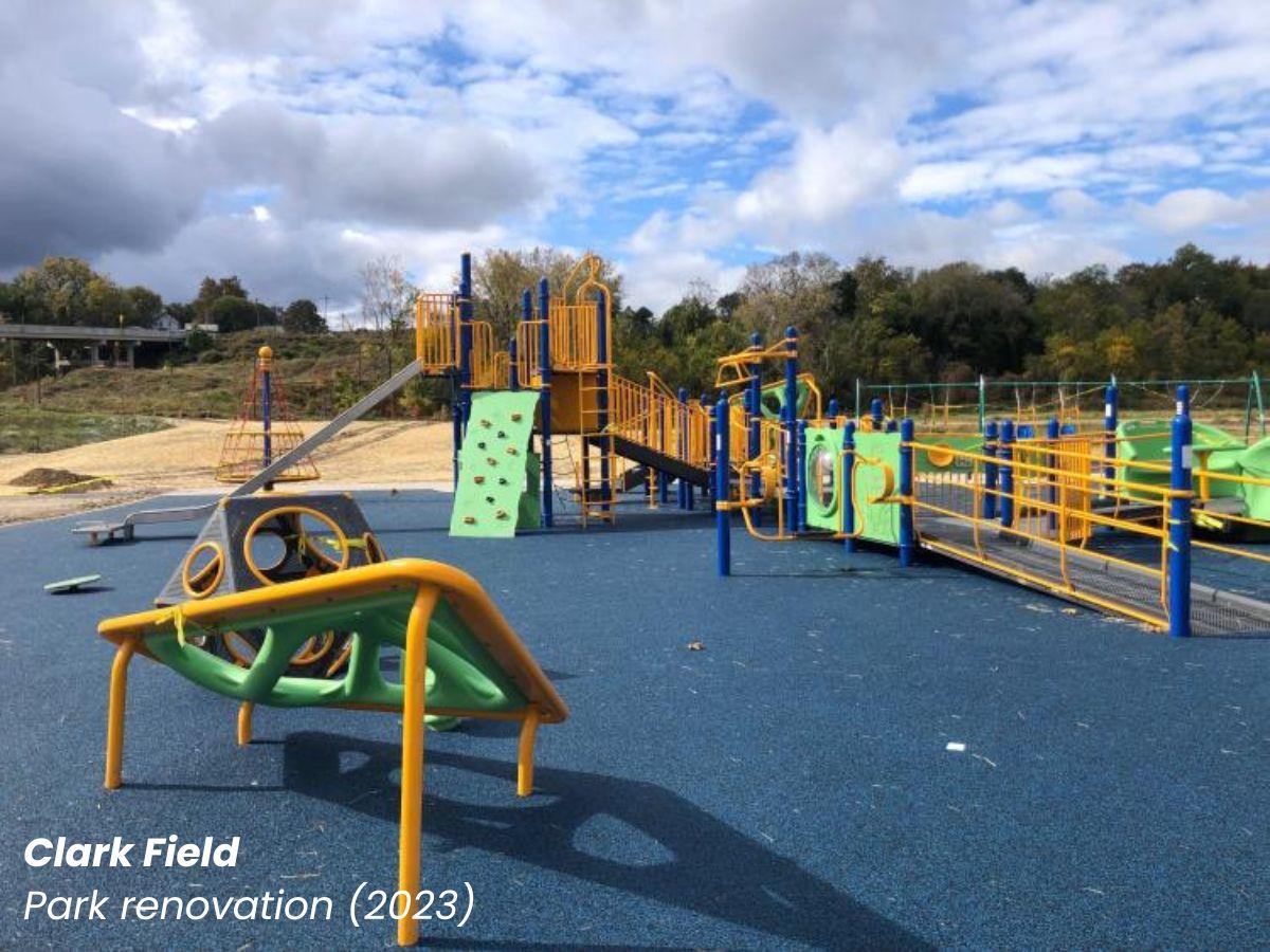 Clark Field renovation showing a modern yellow and green playground with dense trees in the distant background and a cloudy sky.