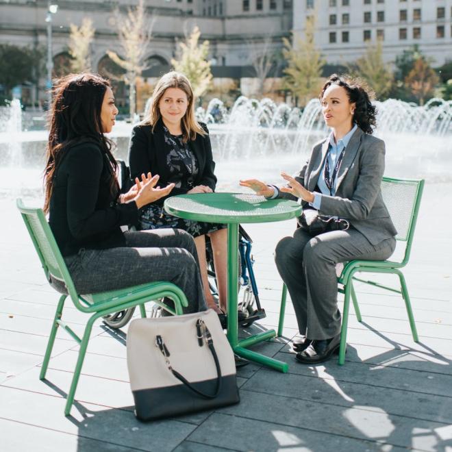 Three women sitting at outdoor table near fountain