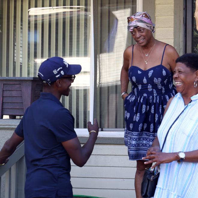 Mayor Justin Bibb smiling and talking to two residents on their front porch.